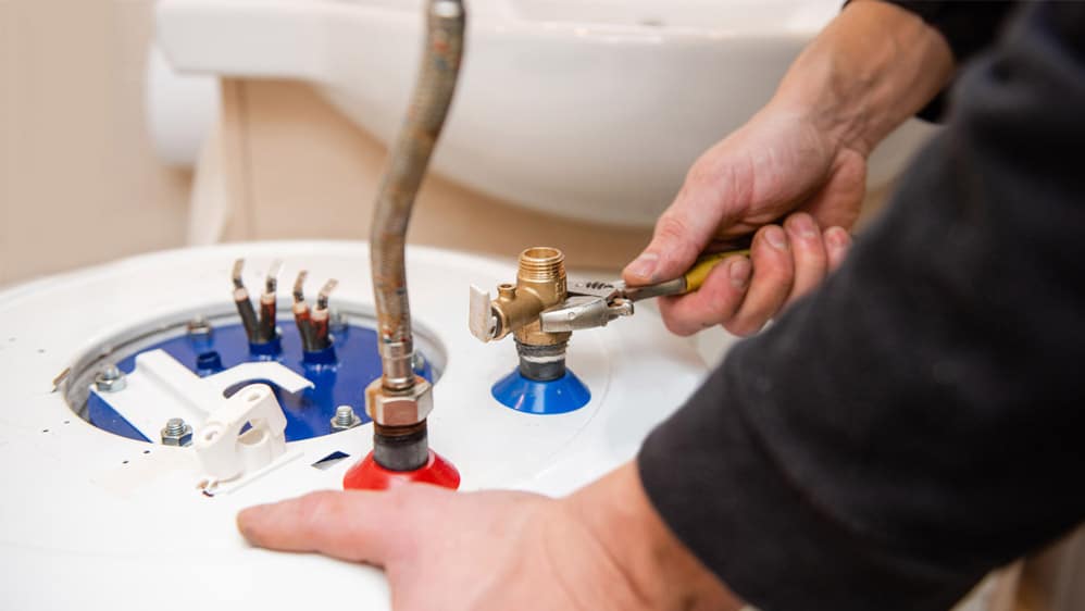 Technician replacing leaking residential water heater in garage utility area